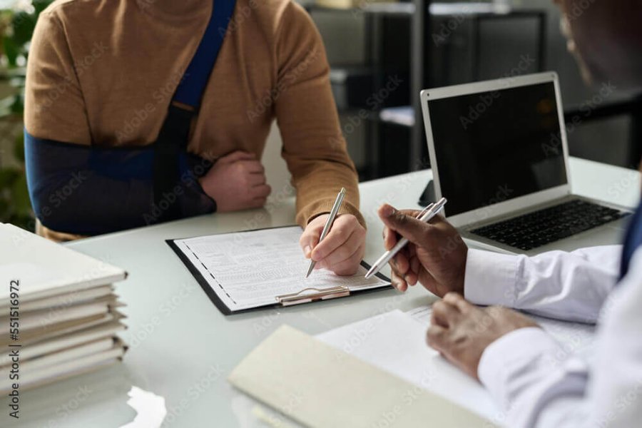 Injured worker with his arm in a sling, signing a legal document with an attorney